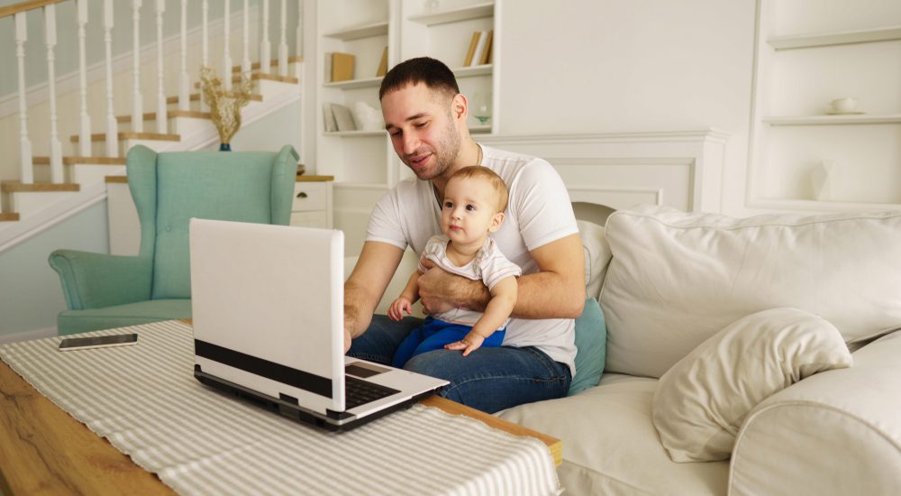 Un uomo davanti al pc con un bambino in braccio